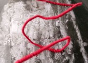 Sur une photo en noire et blanc d'un voile blanc de mariée, un fil rouge s'entrelace.
